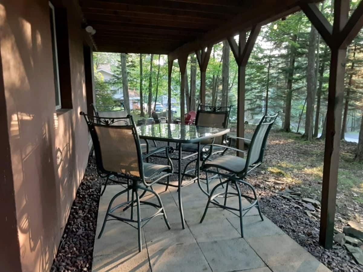 Covered patio seating beneath the cabin deck, surrounded by trees